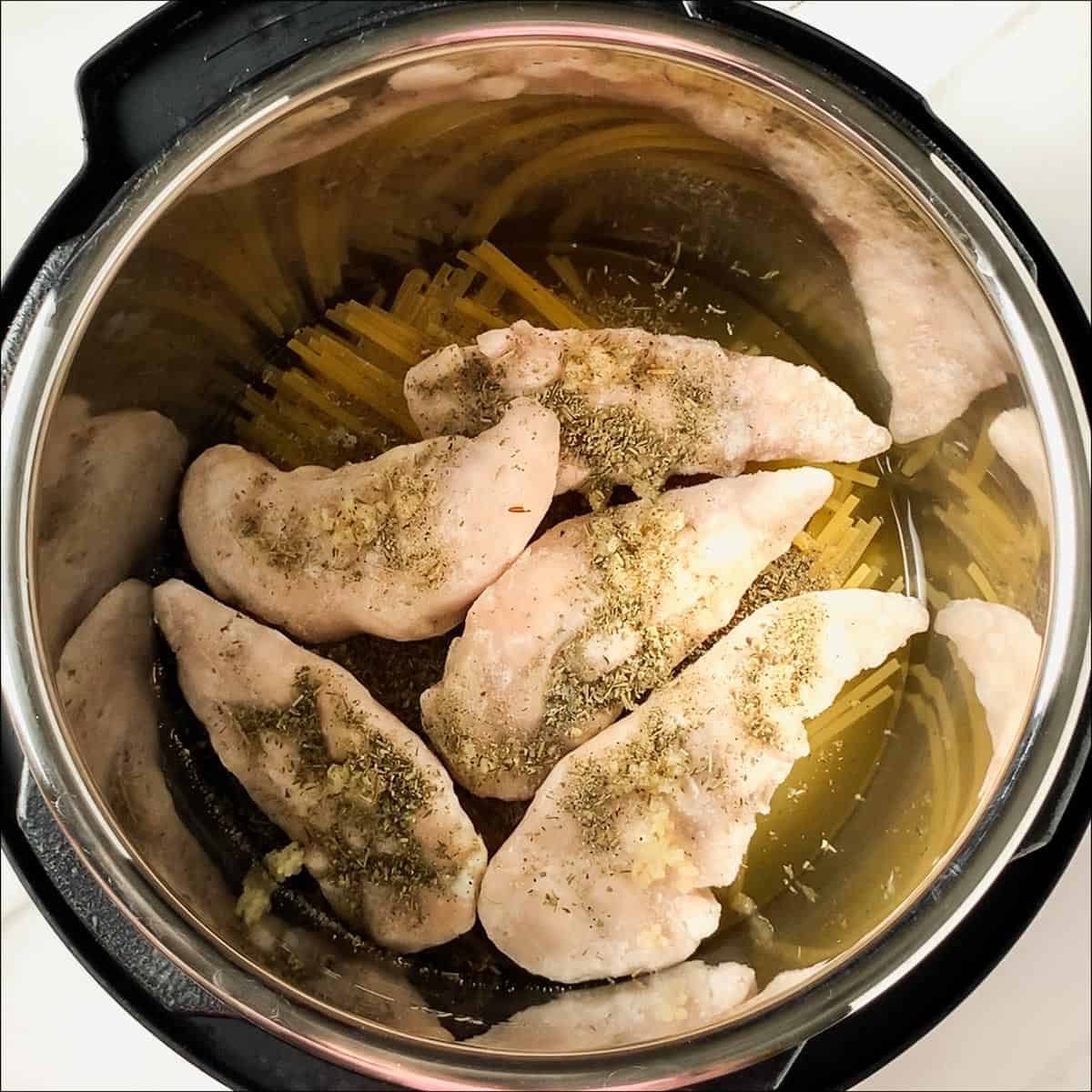 raw frozen chicken tenders and seasoning on top of pasta in instant pot
