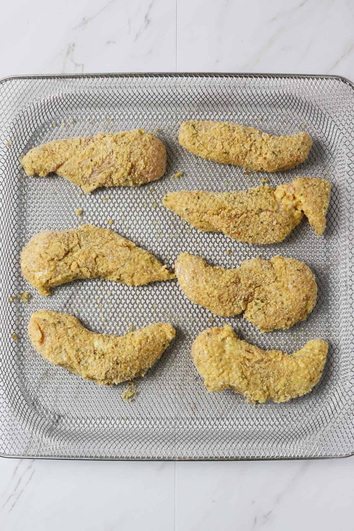 raw chicken tenders with breading in air fryer basket