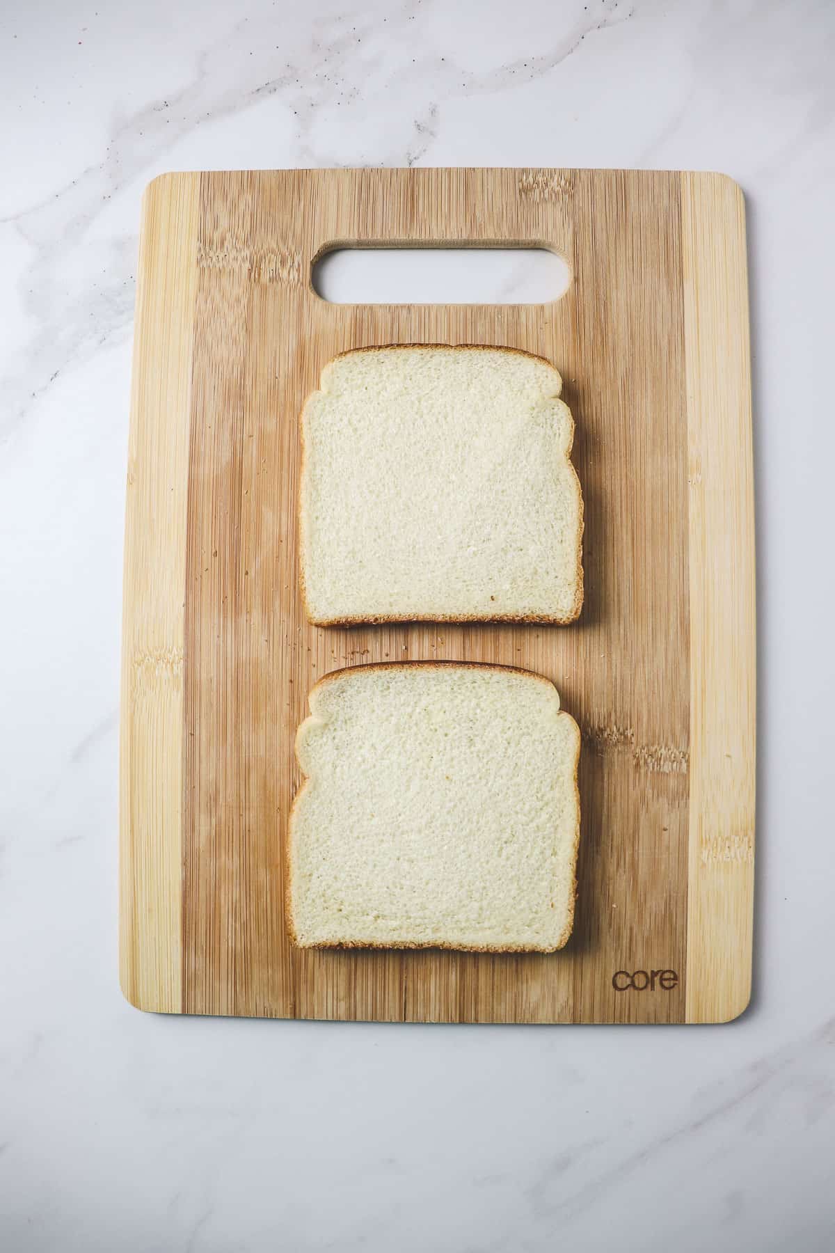 two pieces of white sandwich bread sitting on a wood cutting board