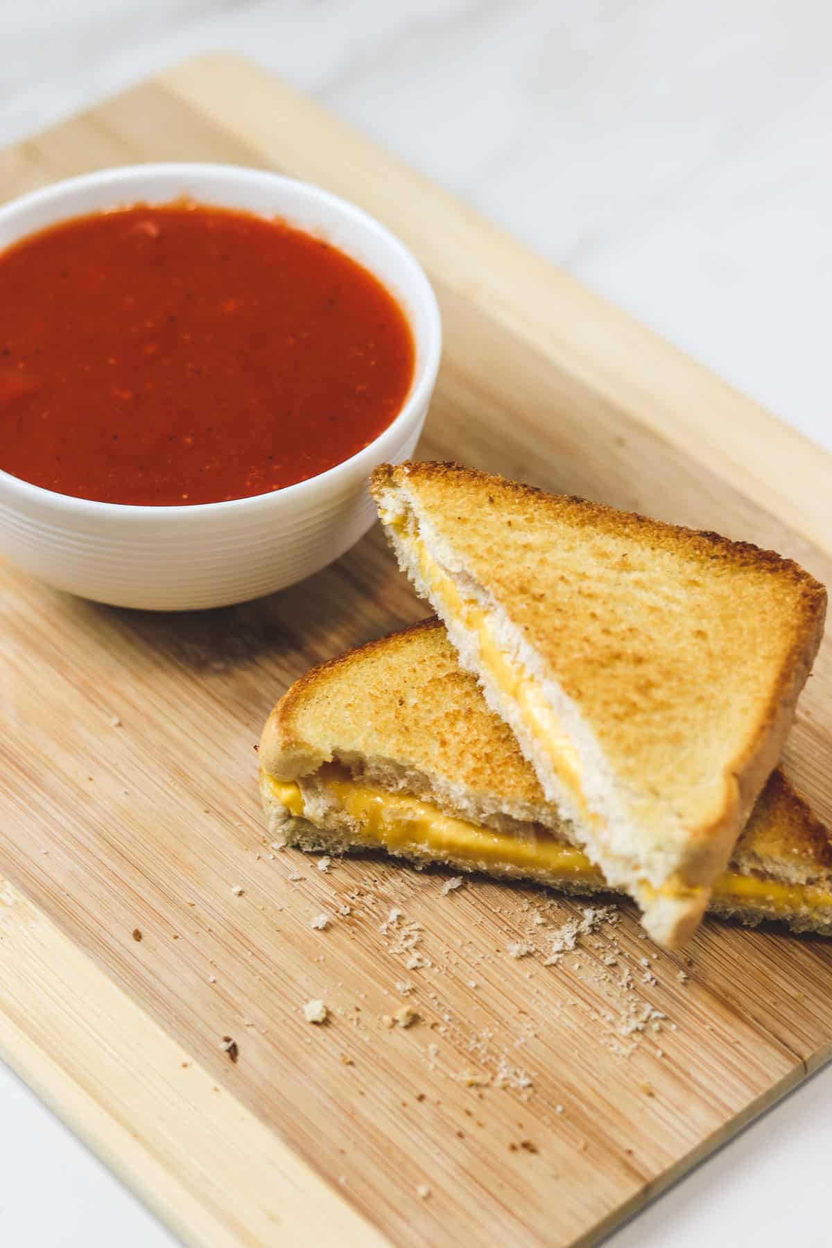 air fryer grilled cheese cut in half with a bowl of tomato soup on a wood cutting board