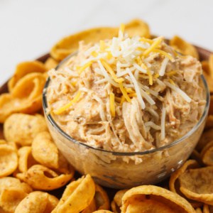 crock pot mexican chicken with shredded cheese on top sitting on plate of corn chips