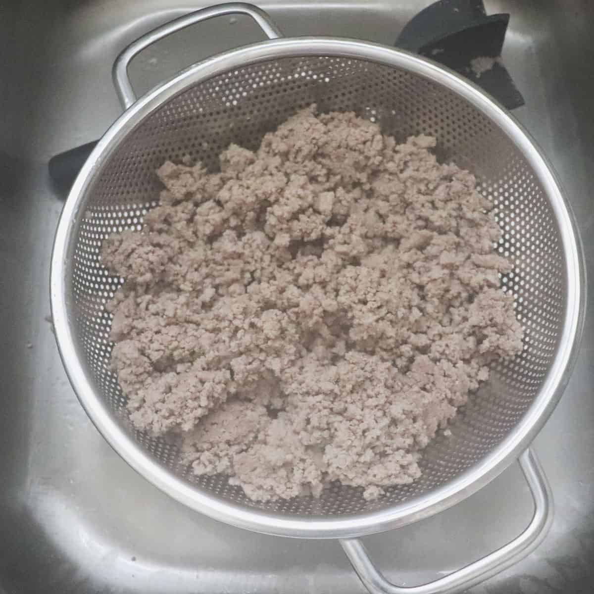 draining ground turkey in metal strainer in sink