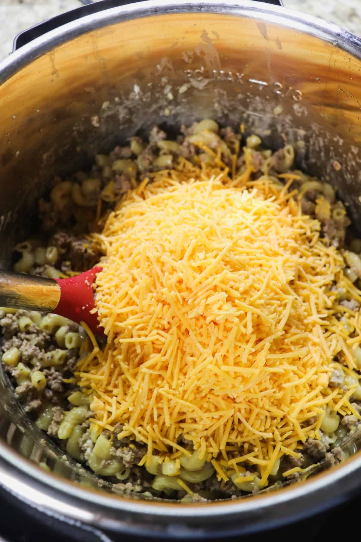 adding shredded cheddar cheese to cooked noodles and ground turkey in instant pot