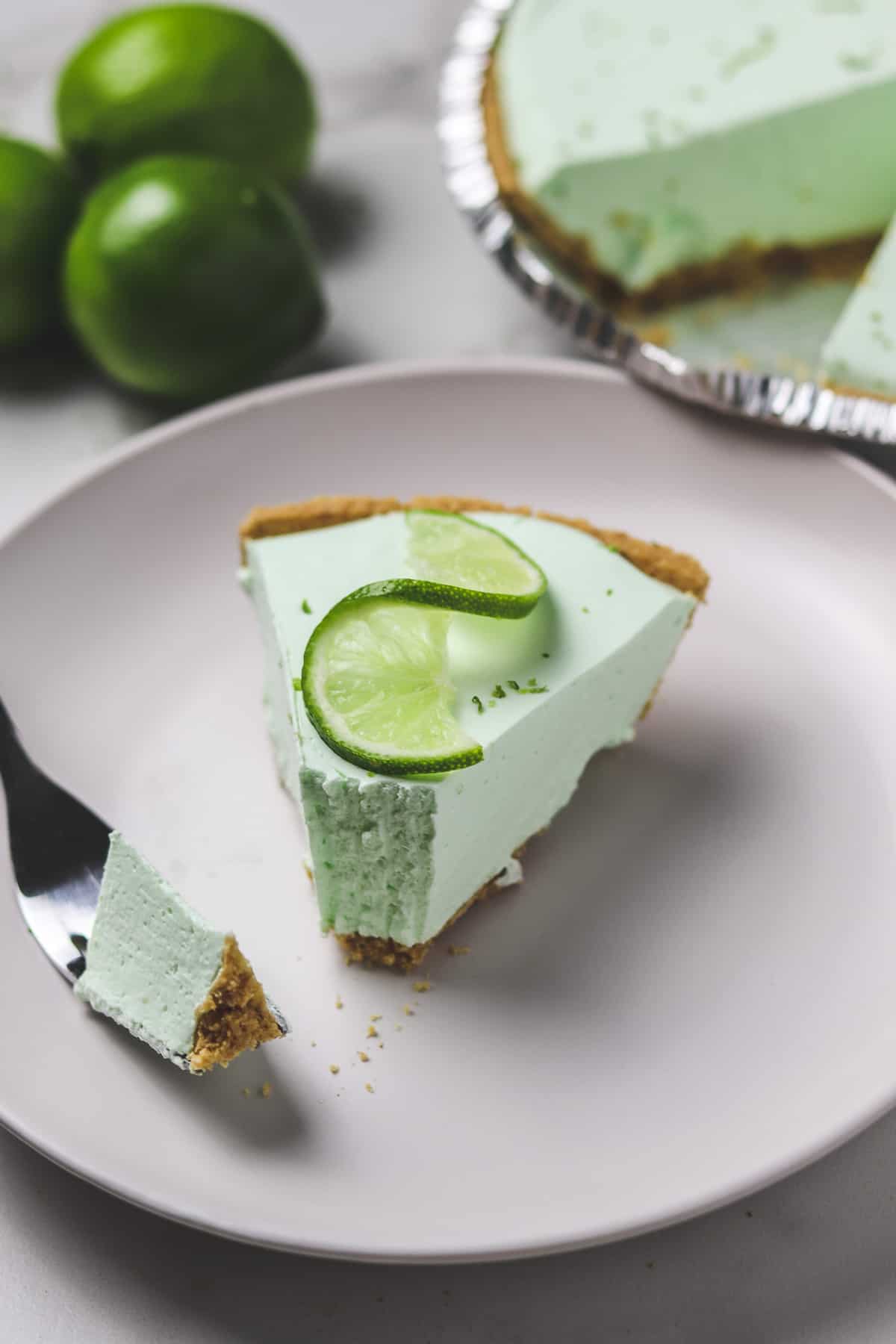 piece of key lime pie on a plate with a bite taken out with a fork