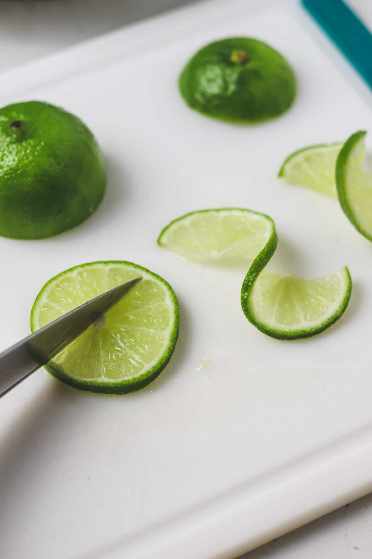 cutting a lime with a knife to make a lime twist on a cutting board