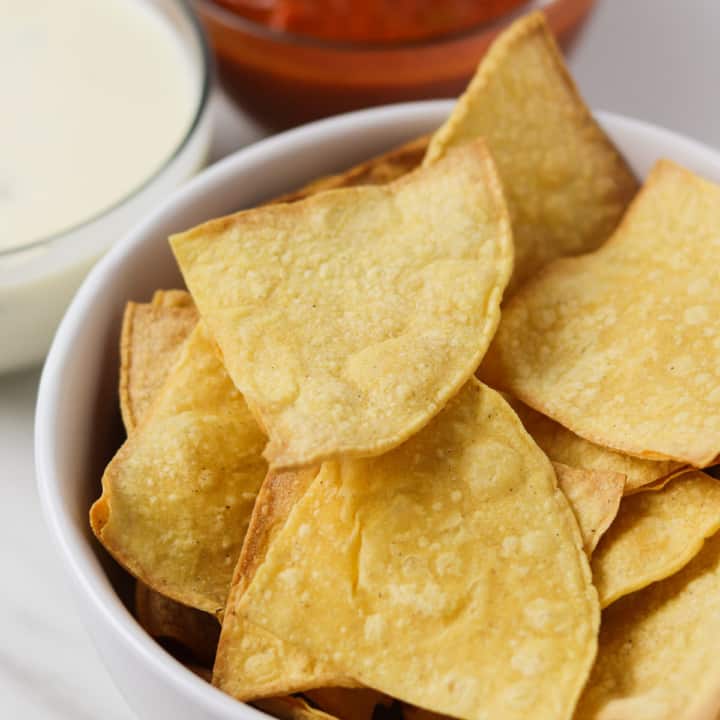air fryer tortilla chips in bowl with salsa and queso in the background