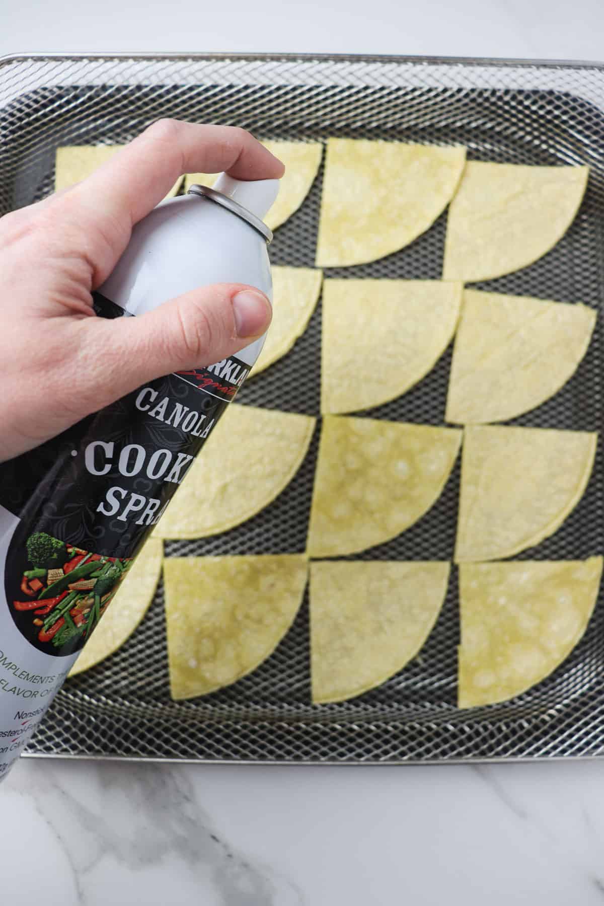 spraying corn tortillas with canola oil in air fryer basket