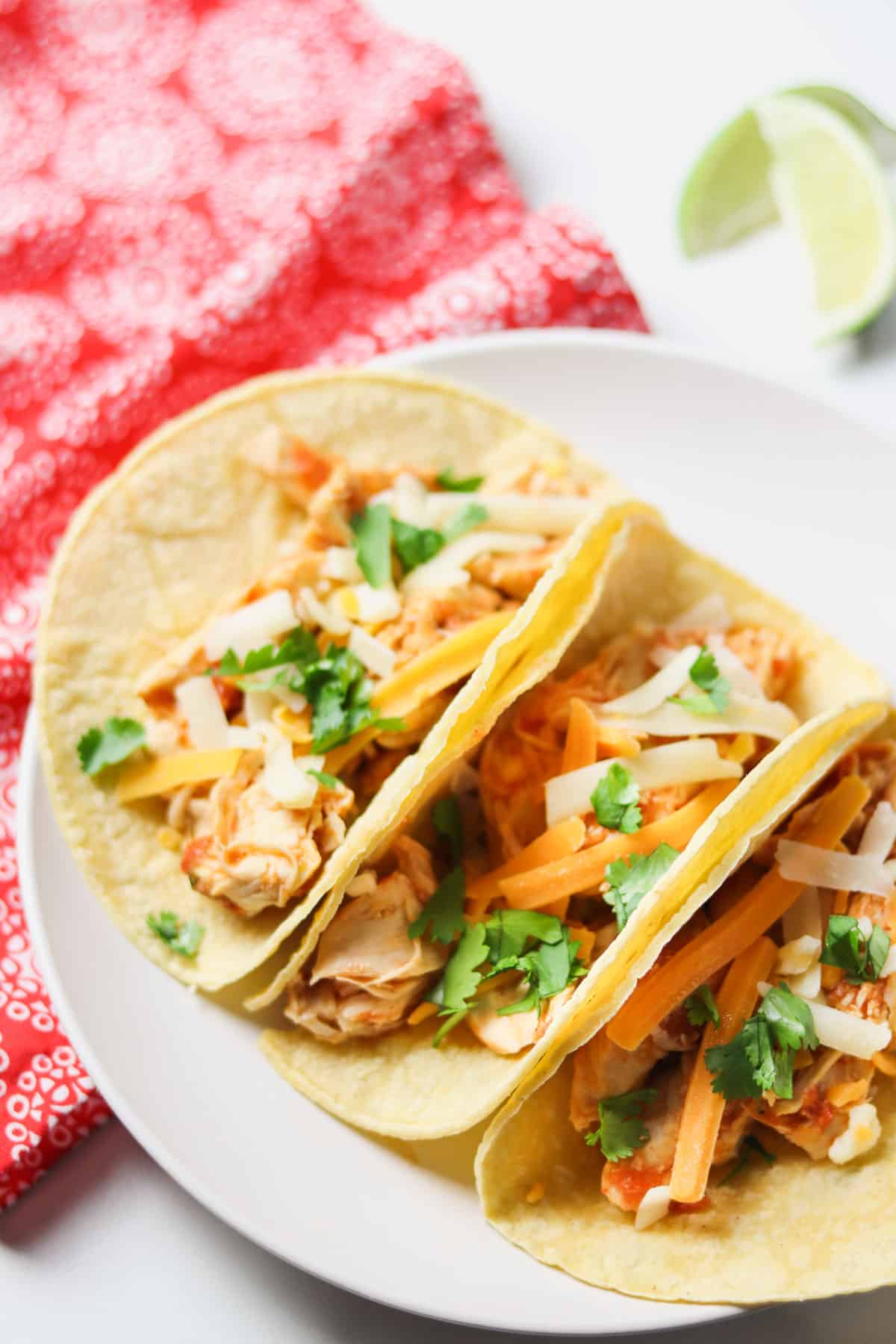 instant pot shredded chicken tacos on white plate with red pattern napkin and limes