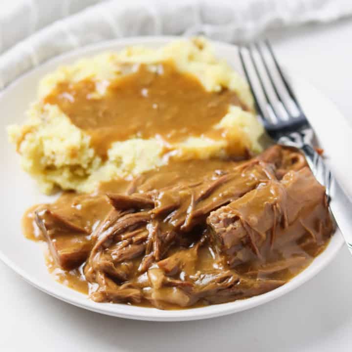 pot roast with gravy on plate with mashed potatoes and fork