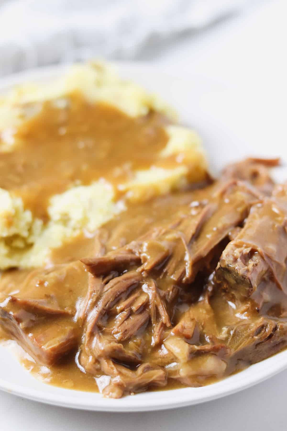 white plate with pot roast and mashed potatoes with gravy