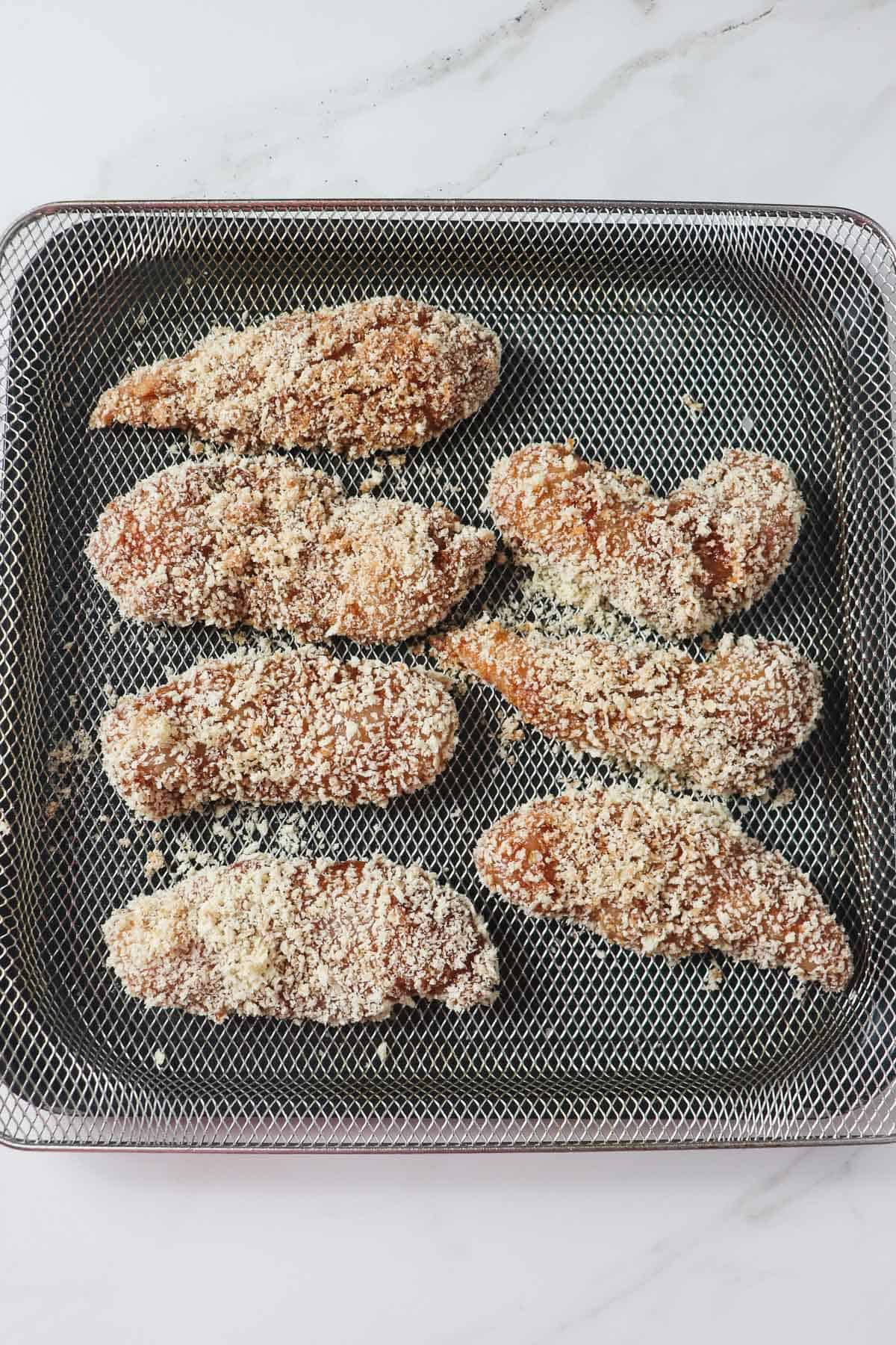 unbaked chicken tenders coated in panko loaded in air fryer basket 