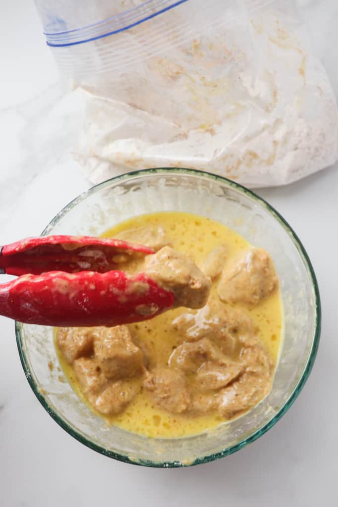 using tongs to dip chicken nugget pieces in egg and milk mixture