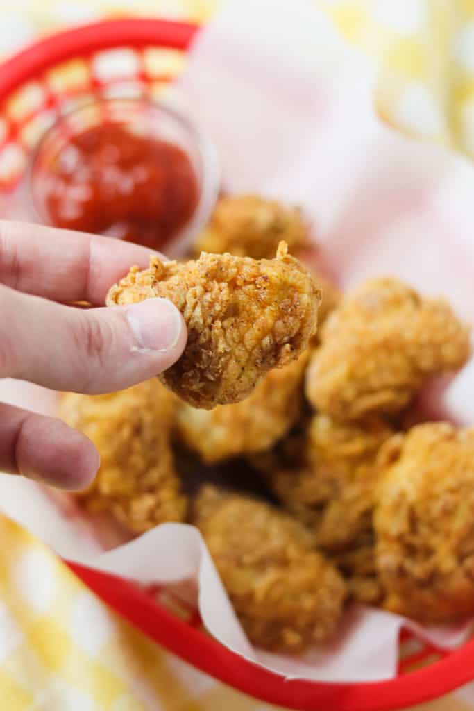 holding up a chicken nugget from a basket of nuggets