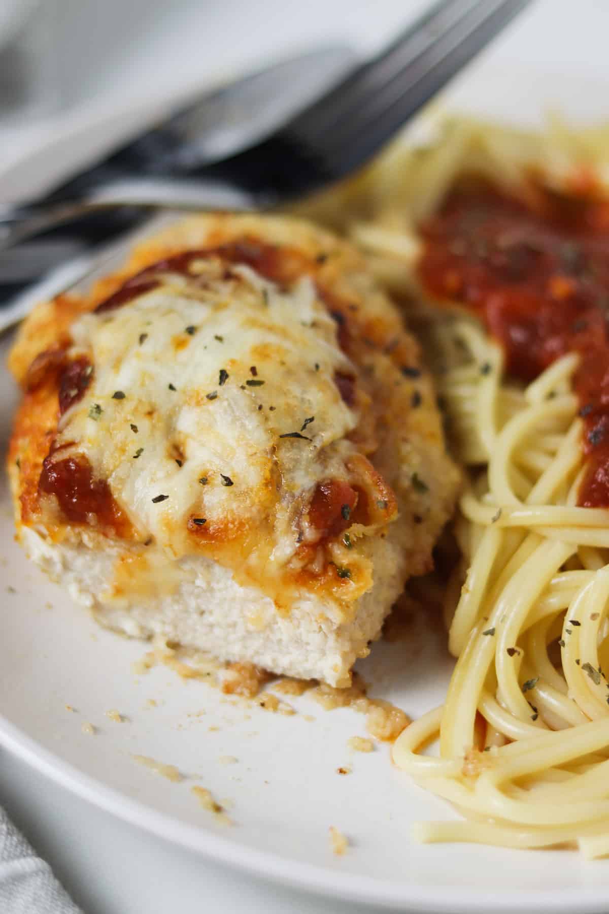 bite taken out of chicken parmesan on white plate