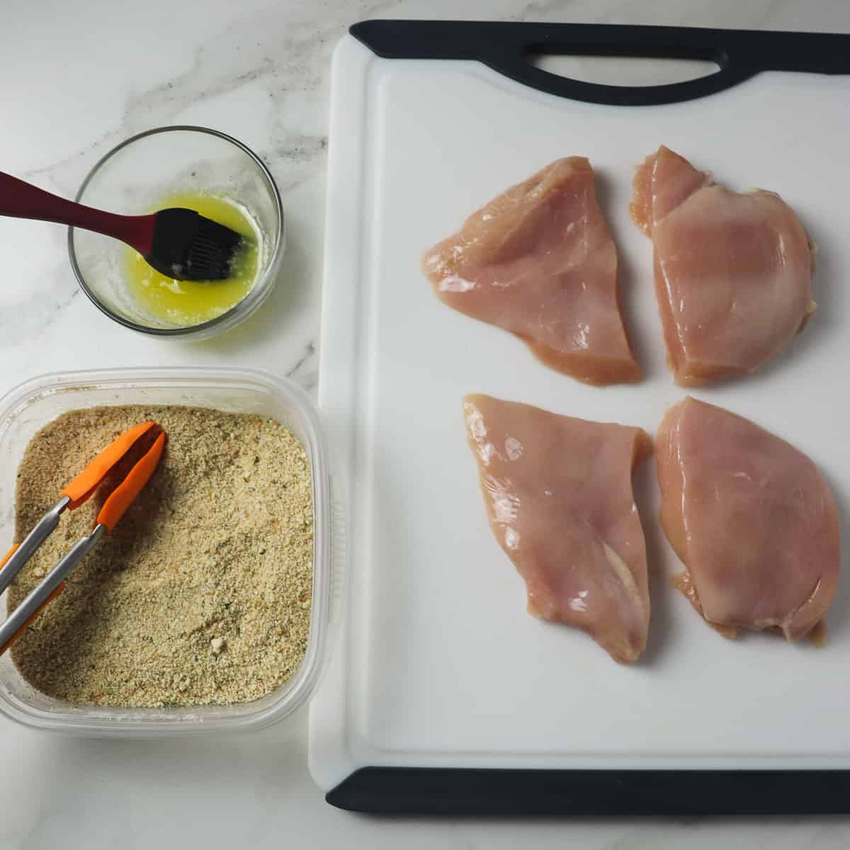 chicken breasts on cutting board with melted butter and parmesan breadcrumb mixture