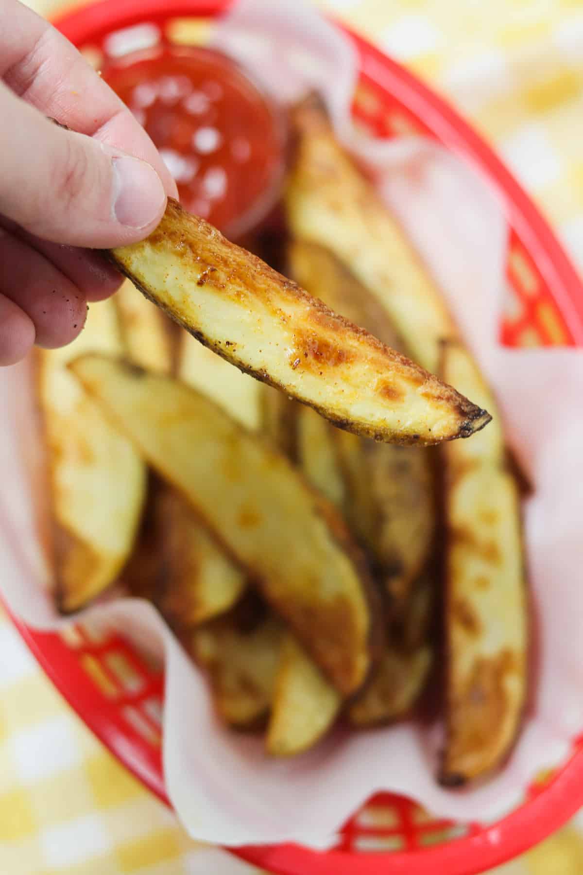 holding an air fryer potato wedge over a basket of wedges