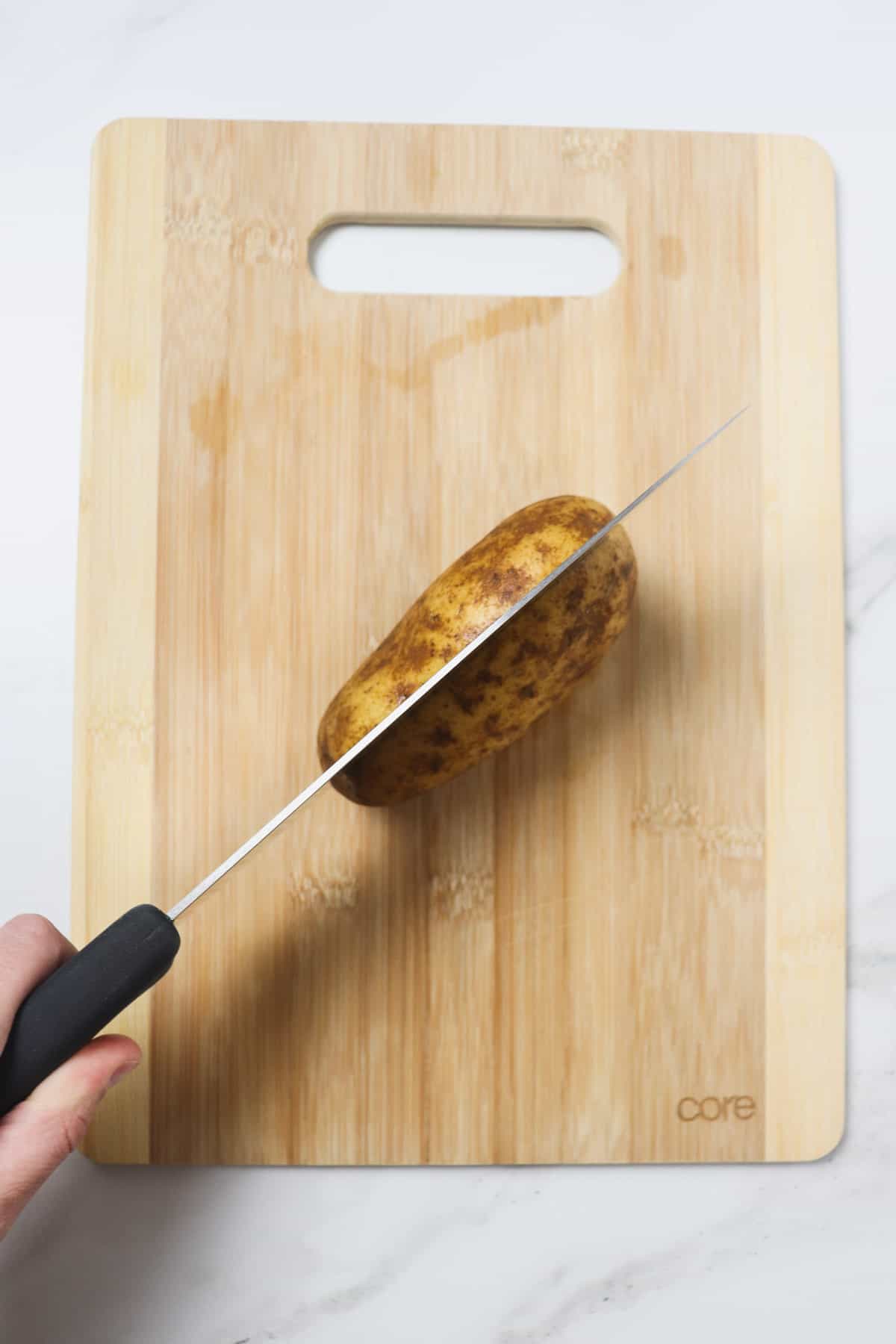 slicing a potato in half on a wood cutting board