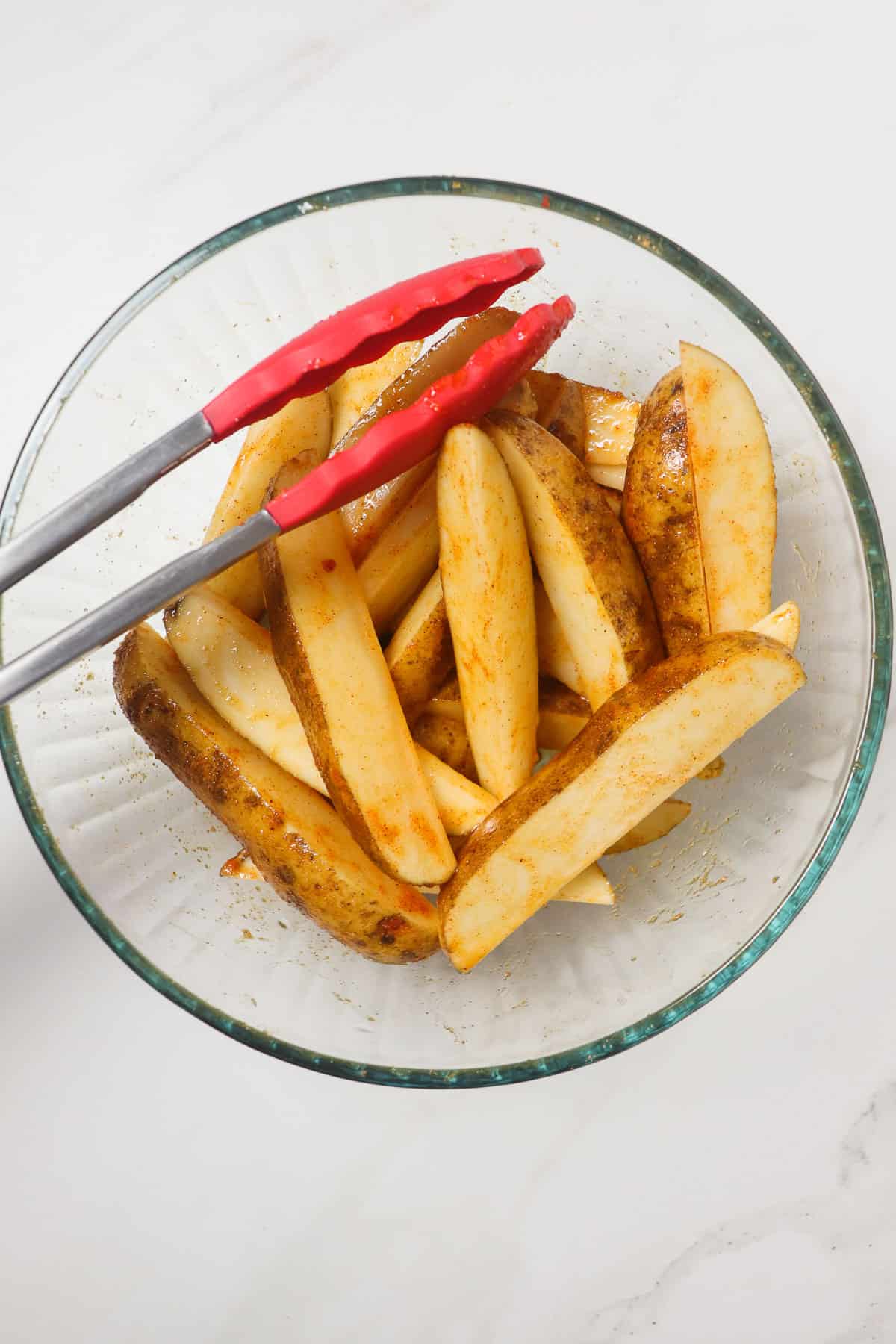 tossing potato wedges in oil and seasoning in a large glass bowl