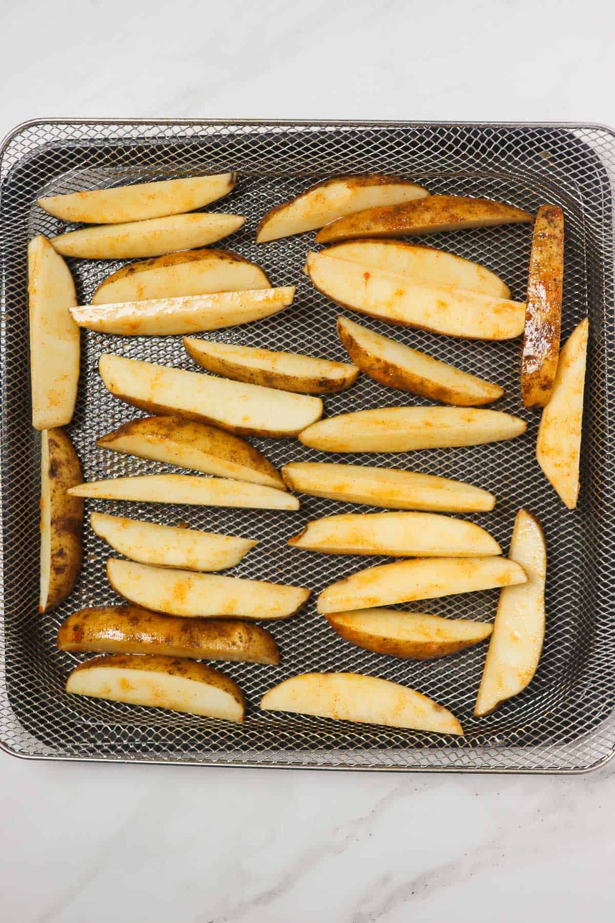 uncooked potato wedges loaded in air fryer basket