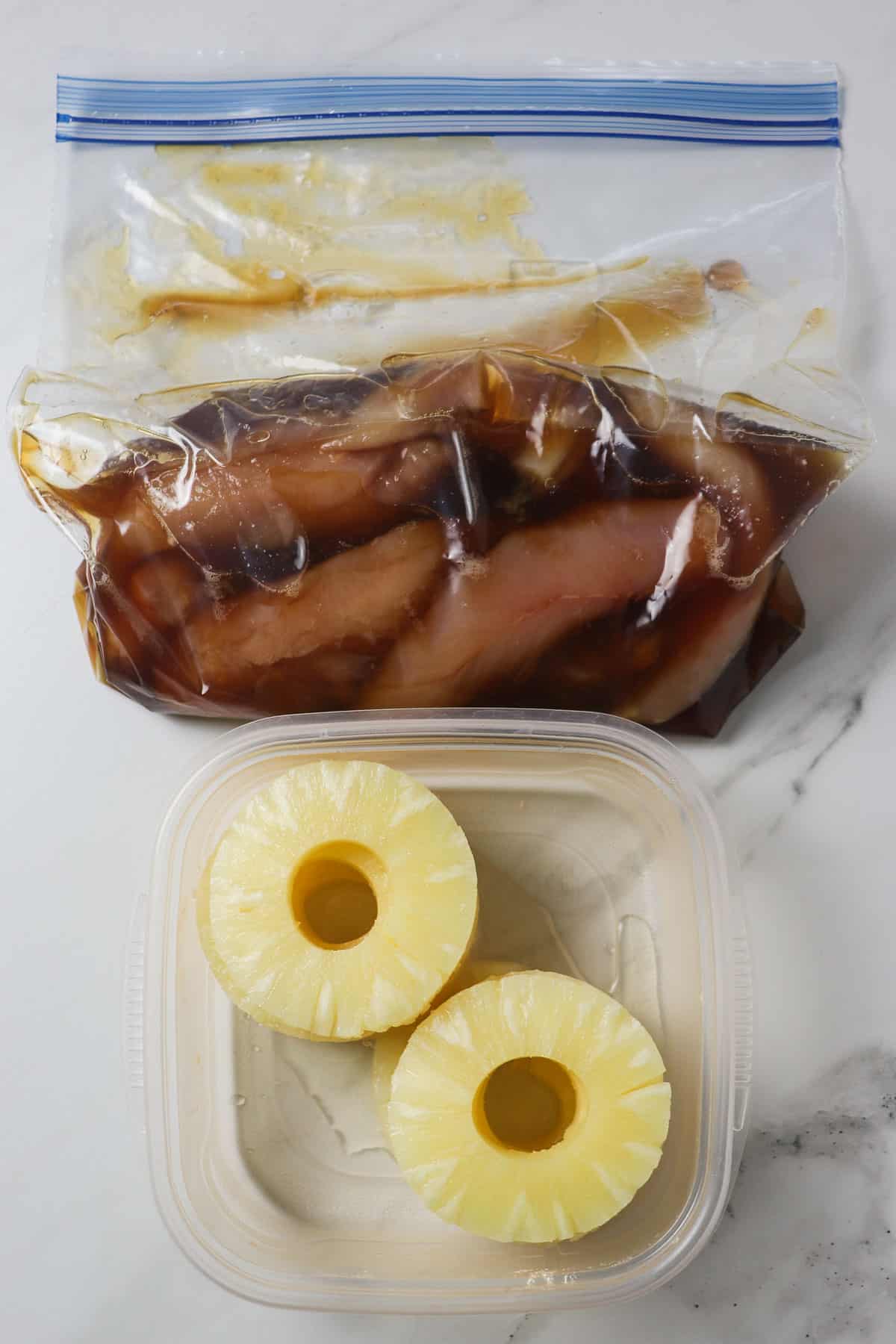 chicken tenders in pineapple marinade with pineapple rings set aside in a plastic container