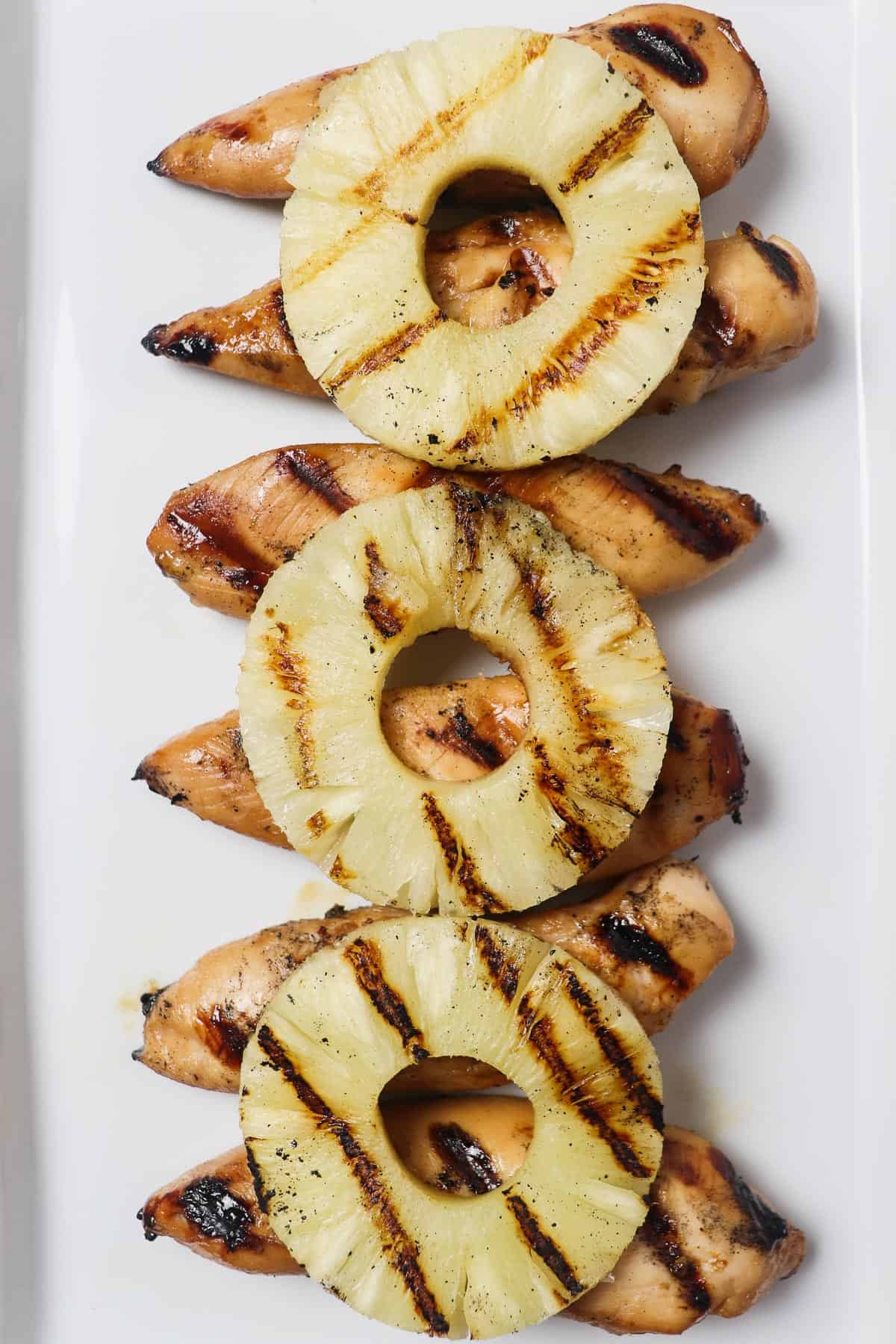 grilled chicken tenders with grilled pineapple rings on a white platter