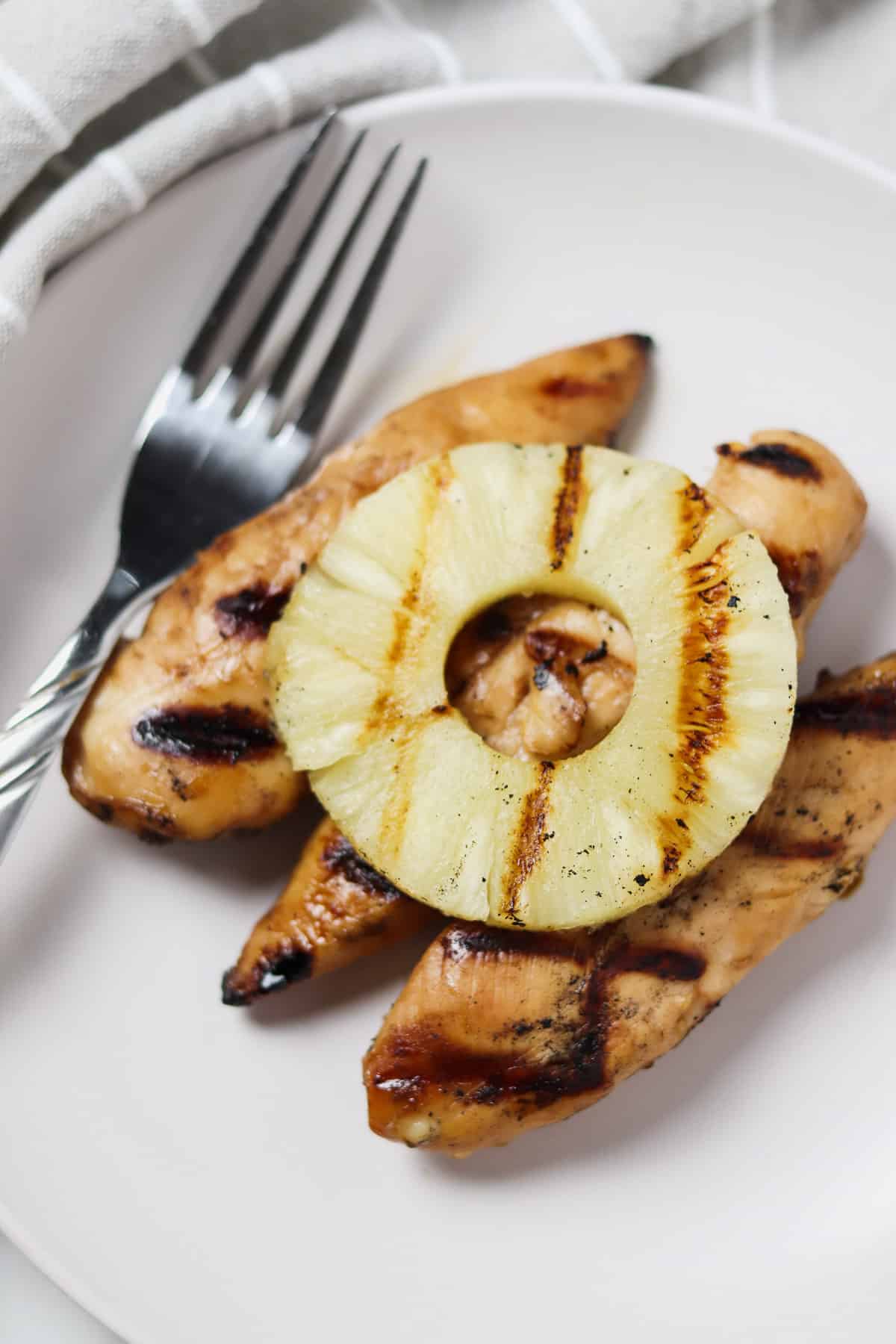 a serving of grilled pineapple chicken tenders on a white plate with a fork