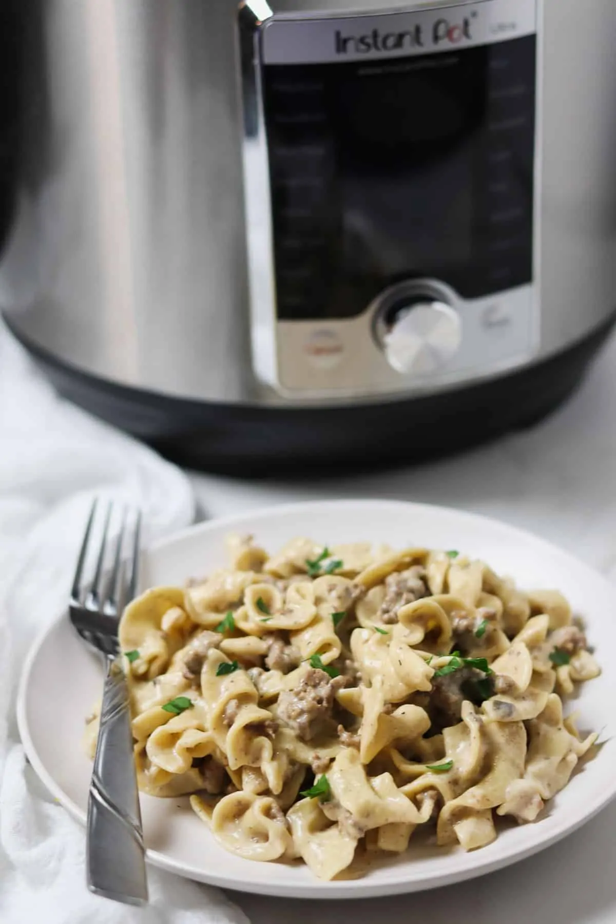 ground beef stroganoff on a white plate with fork with the instant pot in the background