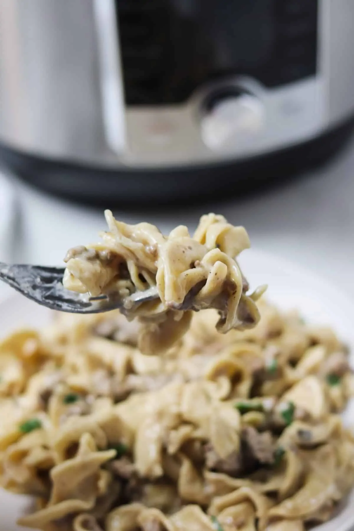 taking a bite of ground beef stroganoff with an instant pot in the background