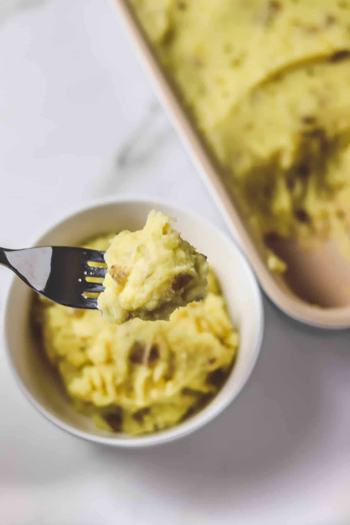 using a fork to take a bite out of a bowl of instant pot mashed potatoes