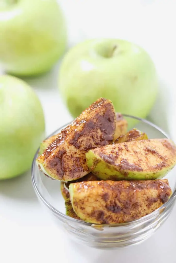 small glass bowl of cinnamon sugar apple slices with green apples in the background