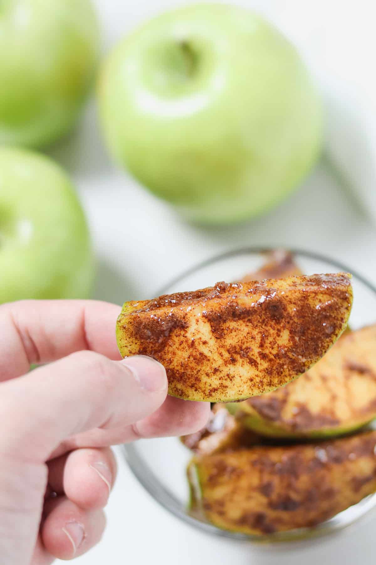 hand holding a cinnamon sugar apple slice with apples in the background