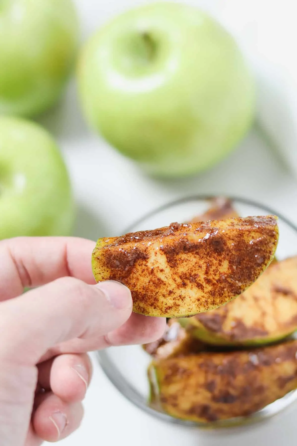 hand holding a cinnamon sugar apple slice with apples in the background