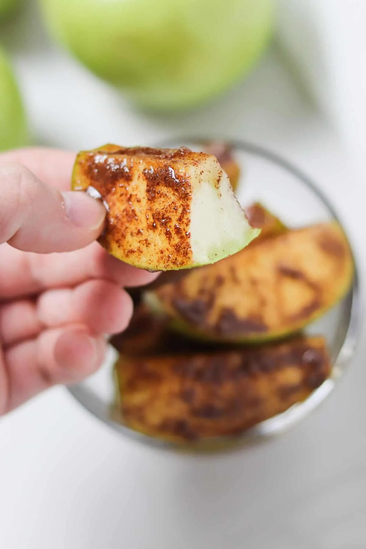 holding an apple slice with a bite taken out of it