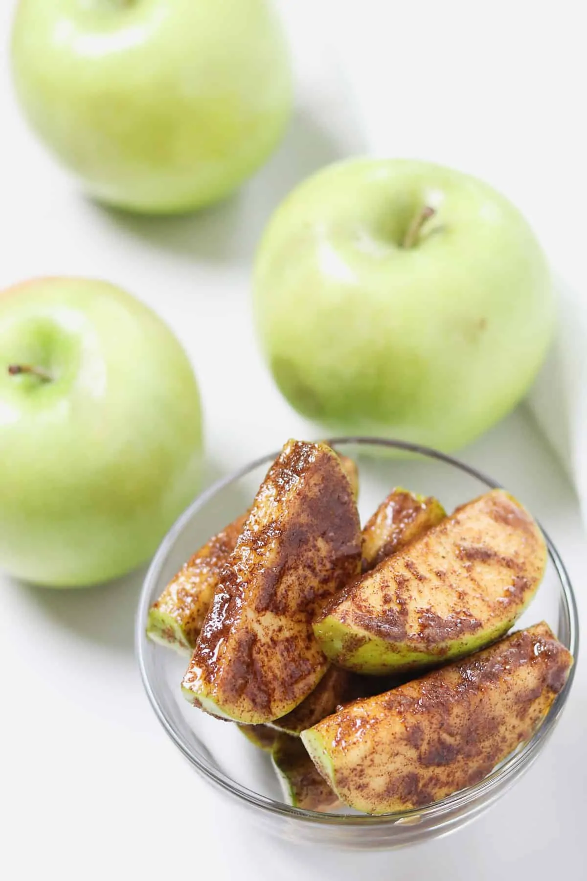 bowl of cinnamon sugar apple slices with green apples in the background