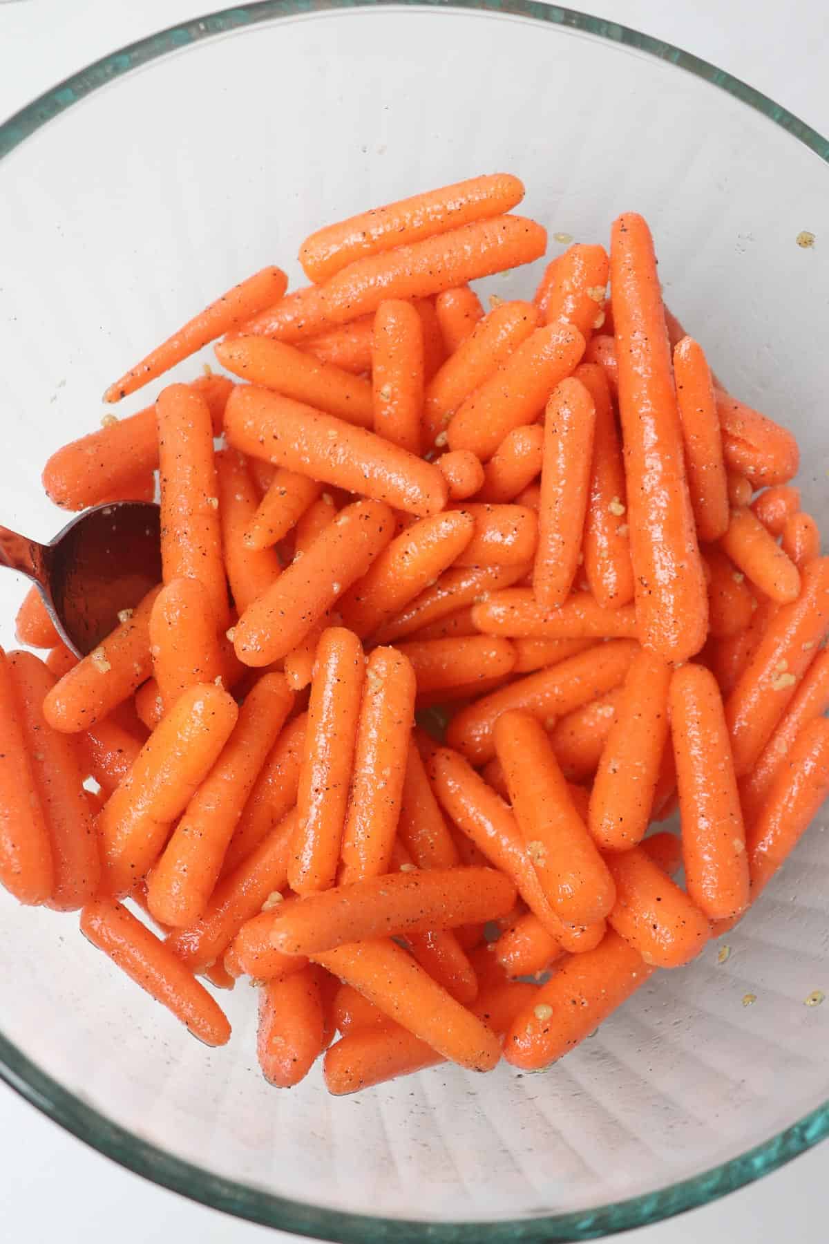 mixing baby carrots with olive oil and seasonings in a glass bowl