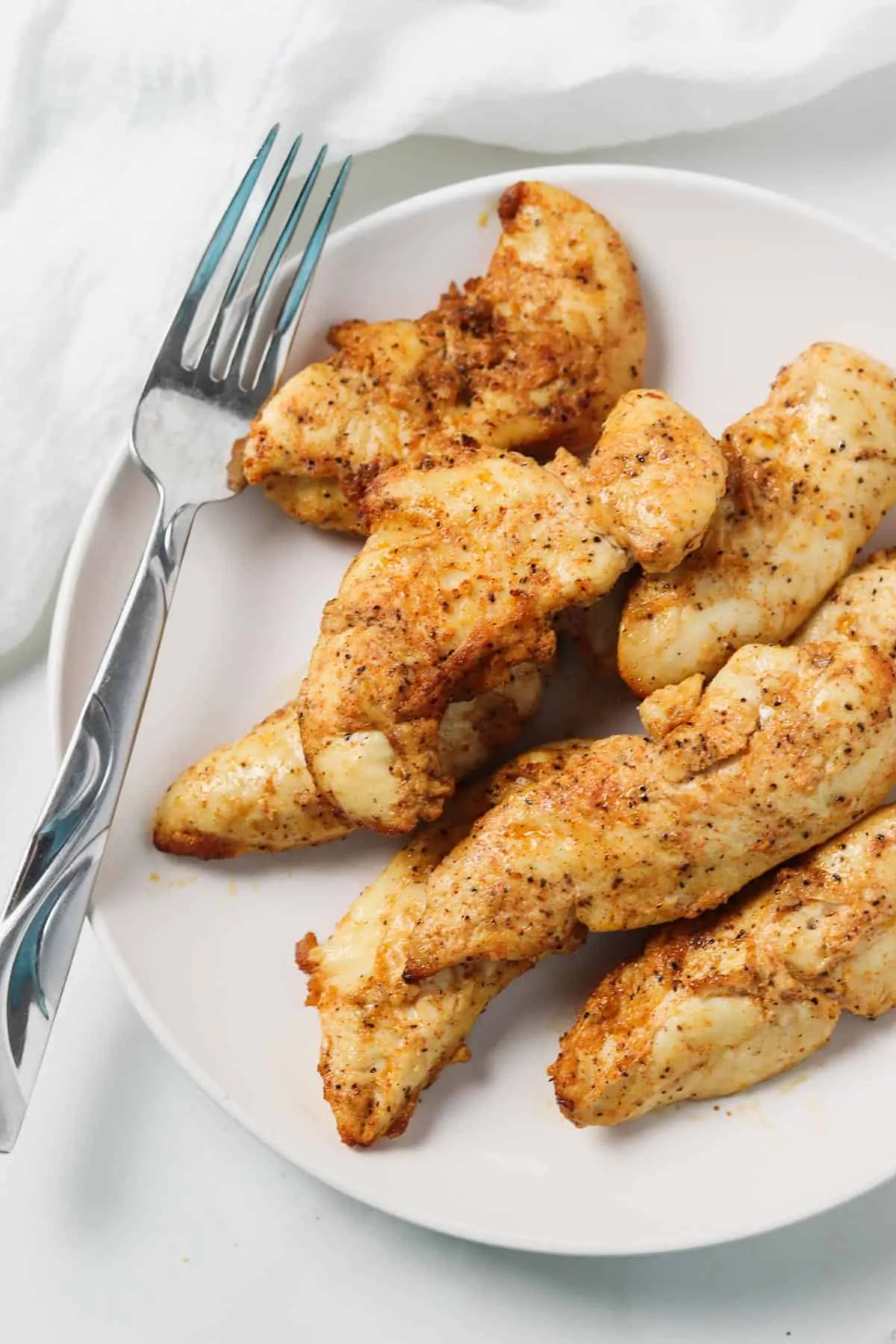 white plate with air fried chicken tenders with fork