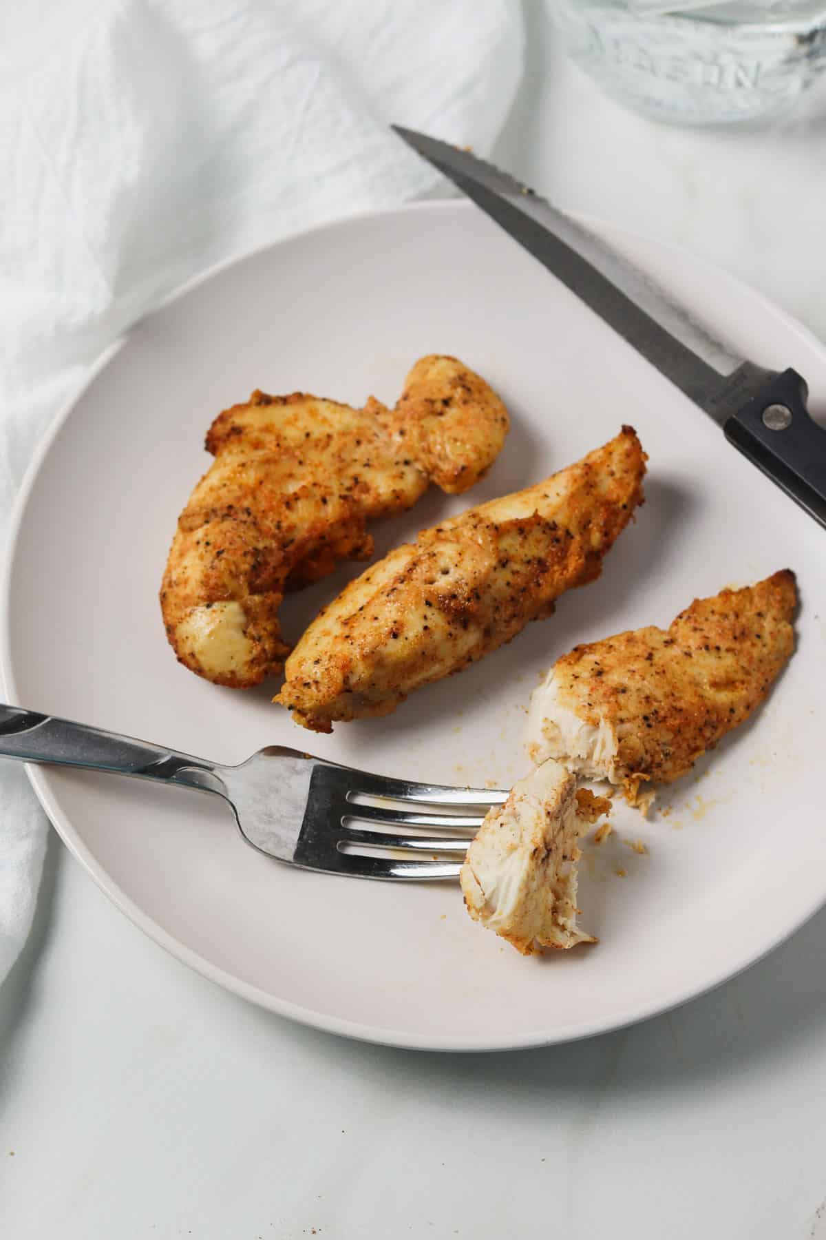 air fryer naked chicken tenders on a white plate with a bite on a fork