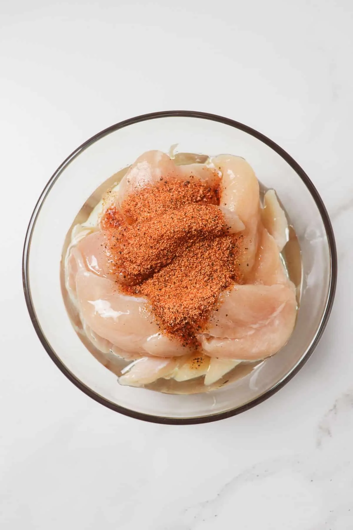 raw chicken tenders with oil, vinegar, and seasoning added to glass bowl