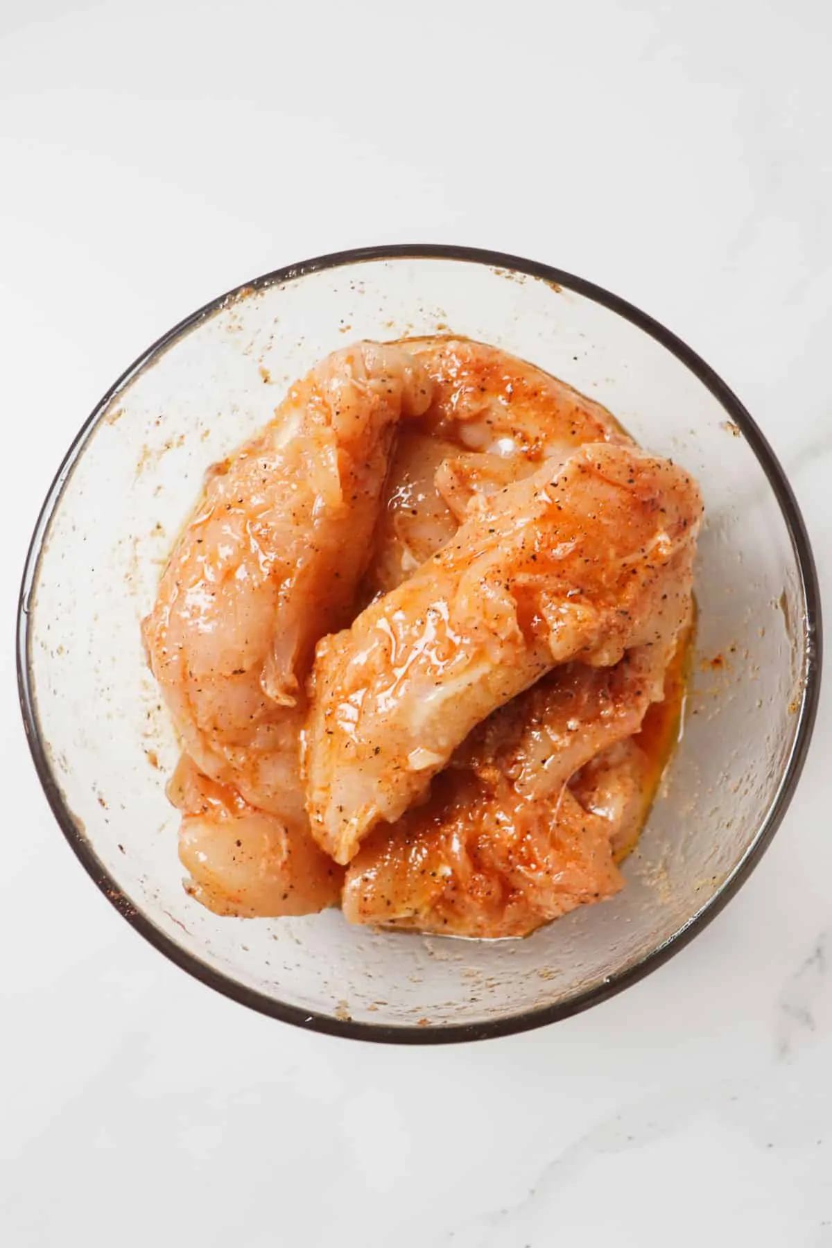 raw chicken tenders marinating in glass bowl