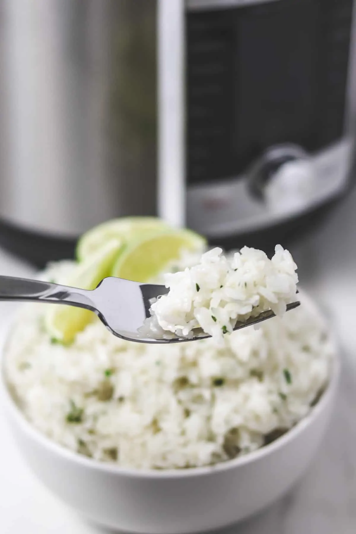 bite of cilantro lime rice on fork in front of bowl of rice and instant pot