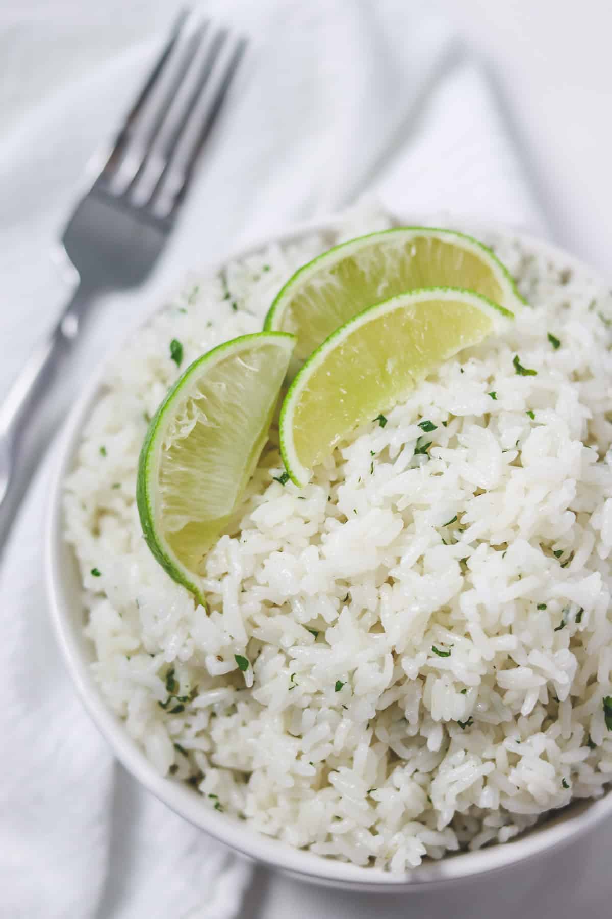 cilantro lime rice in bowl with lime wedges on top with fork