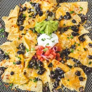 top down view of air fryer nachos in basket with toppings