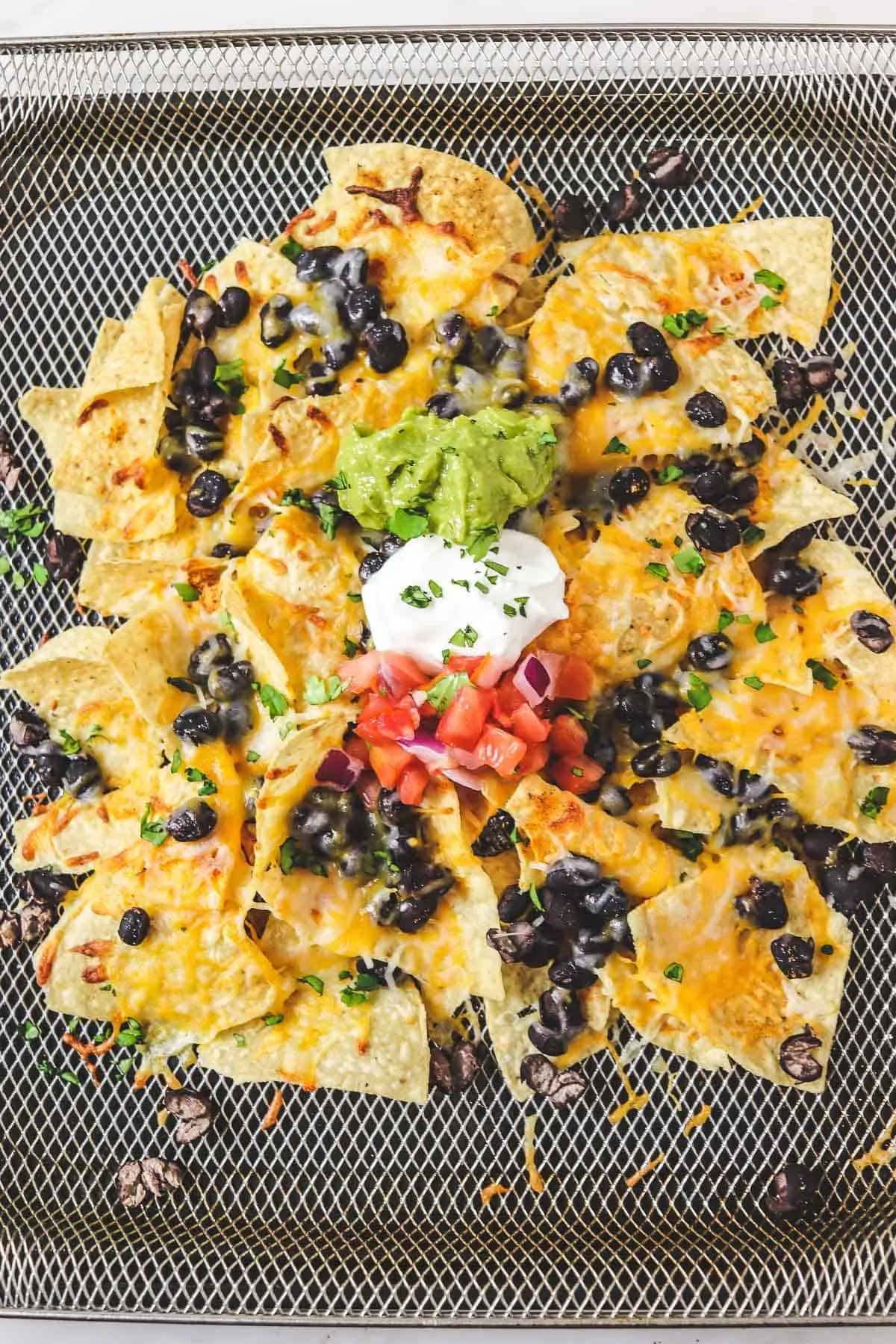 top down view of air fryer nachos in basket with toppings