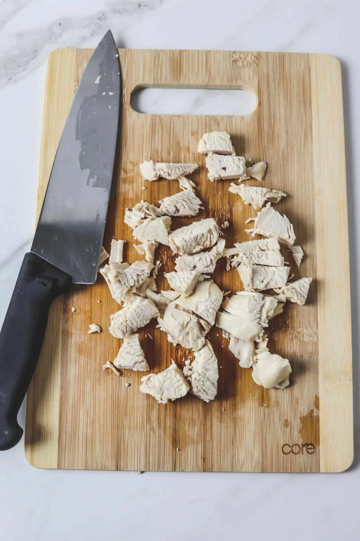 diced chicken breast on a wood cutting board with chef knife
