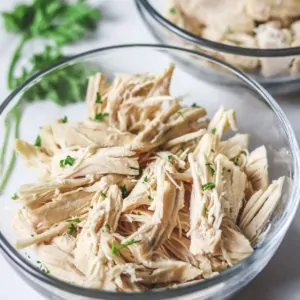 shredded chicken in a glass bowl garnished with parsley