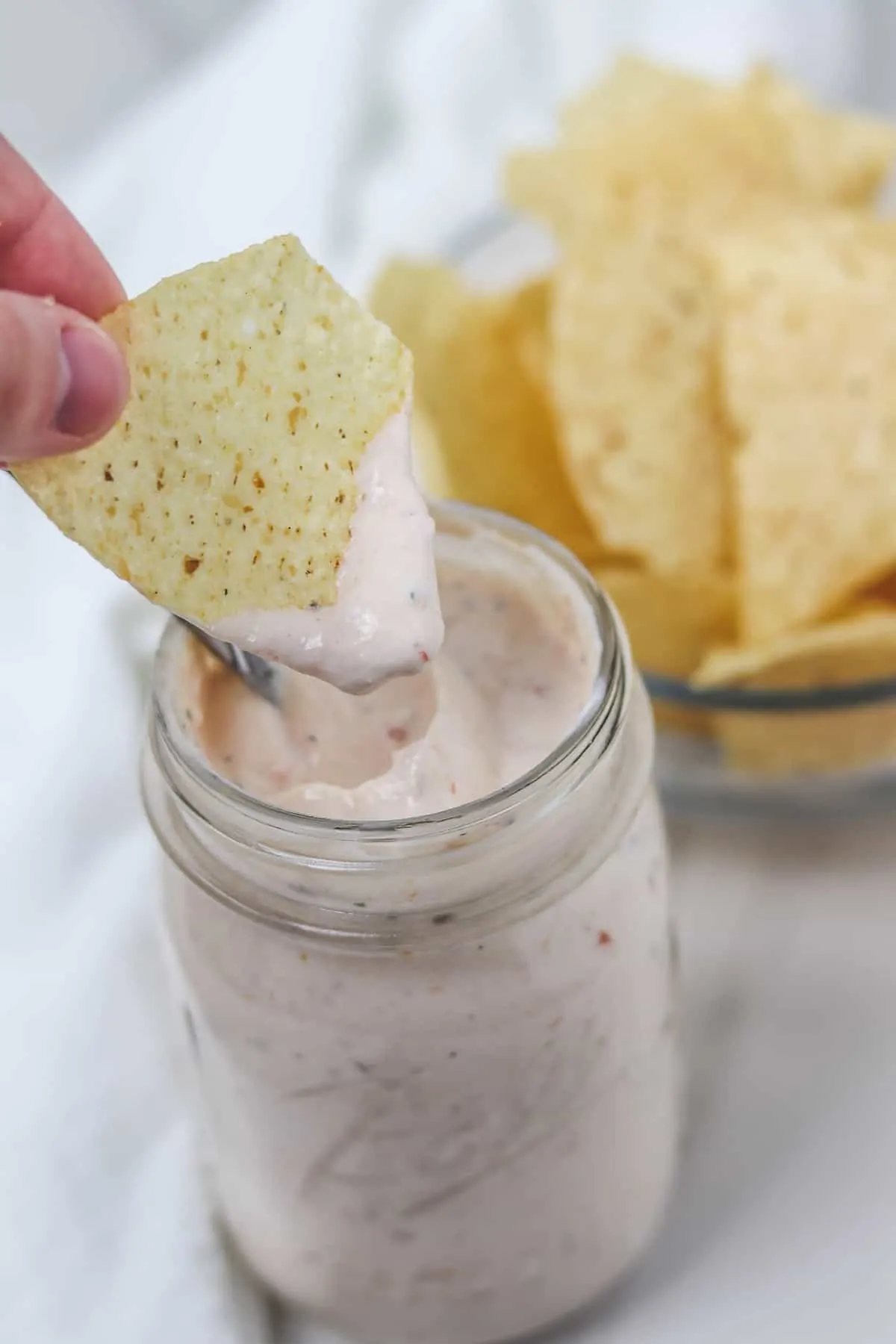 dipping a tortilla chip with salsa ranch dressing from a mason jar