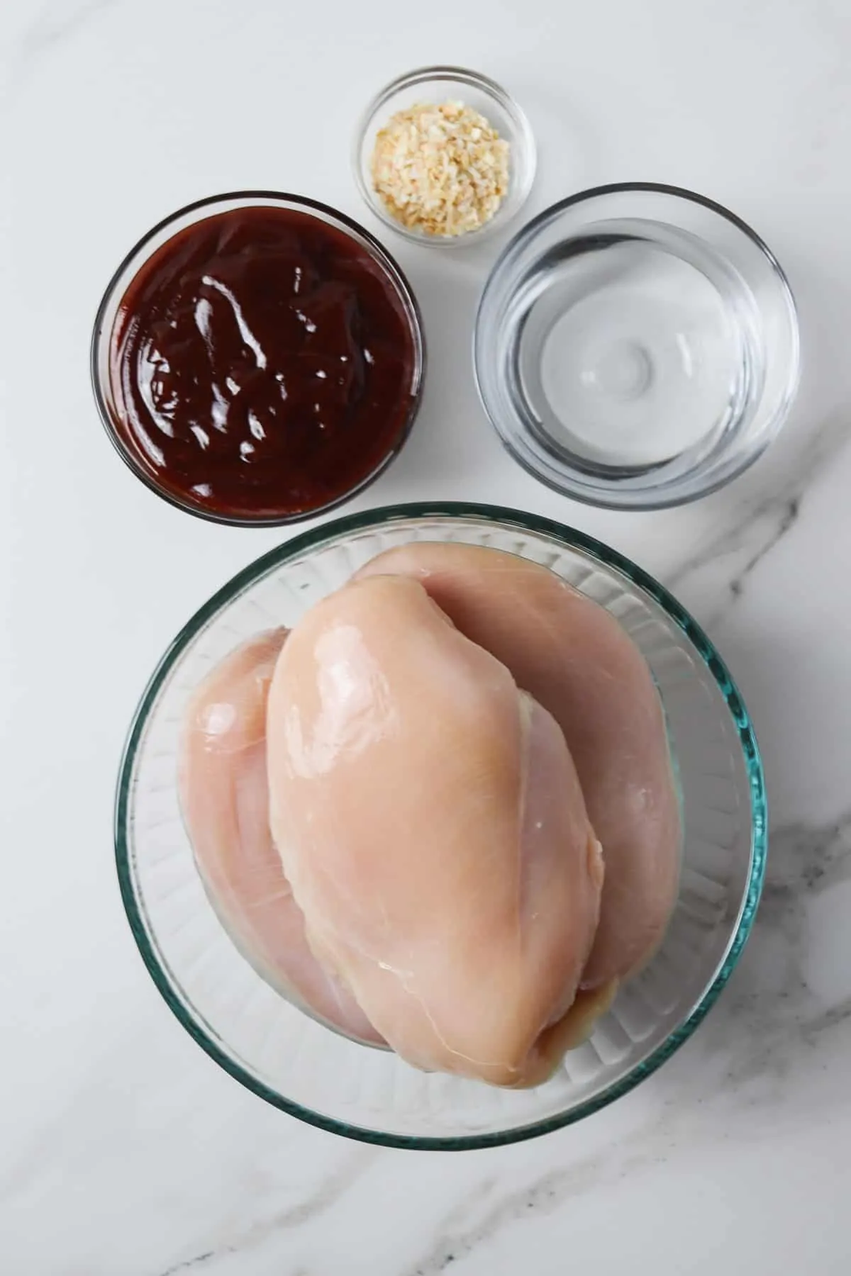 ingredients in instant pot barbeque chicken - chicken breasts, water, bbq sauce, and dry minced onion