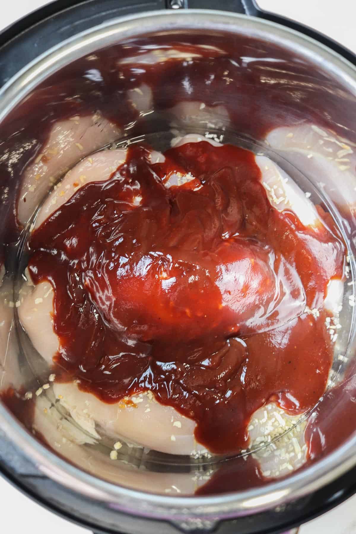 uncooked chicken breasts and bbq sauce in the instant pot liner