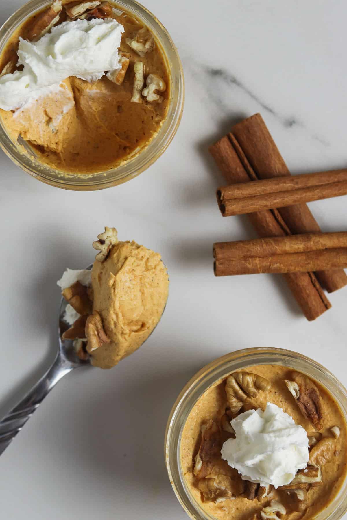two jars of skinny pumpkin fluff with cinnamon sticks and a bite in a spoon