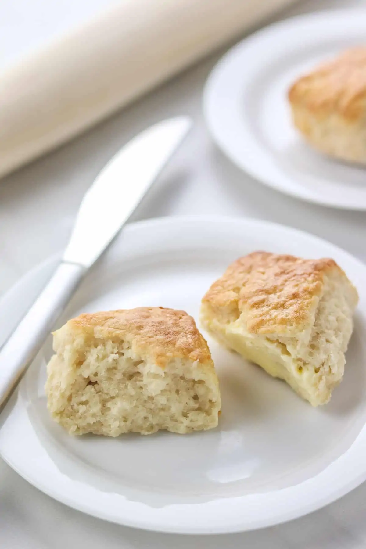 biscuit cut in half on a white plate with a knife and rolling pin